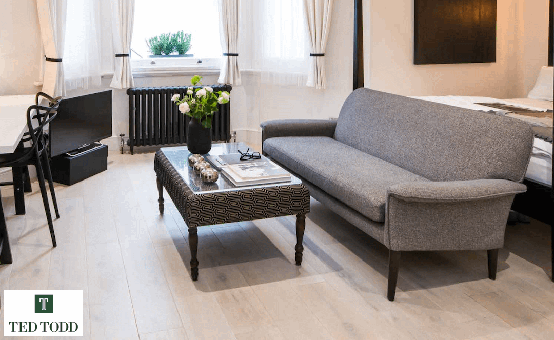 Light coloured Ted Todd Calico European Oak flooring, in a contemporary living room setting under a light grey low backed sofa and matching coffee table.