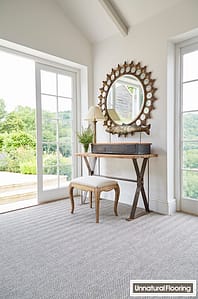 Light grey coloured Unnatural Flooring Bar Harbor fitted carpet in a contemporary bedroom setting featuring double French windows, with a wooden dressing table and low level stool beneath a large round mirror.