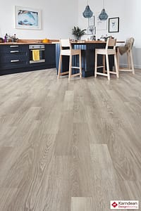 Light coloured Karndean Knight Tile Grey Limed Oak flooring in a contemporary style kitchen dinner with black fronted units and cream wooden bar stools.
