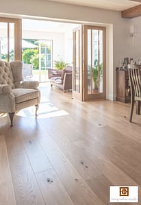 Light coloured V4 Rustic Oak matt lacquered laminate flooring in a contemporary living space with a folding wooden patio doors leading to a conservatory.