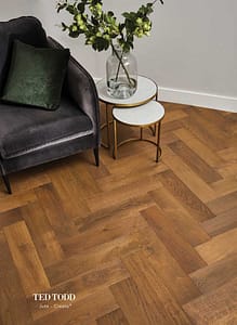 Mixed brown coloured Ted Todd Create Jute parquet style flooring in a contemporary style room under a black leather box chair with nesting metal framed side tables.