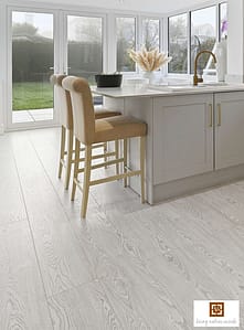 Light coloured V4 Arctic Sky laminate flooring in a modern kitchen with two high backed wooden stools and French doors.