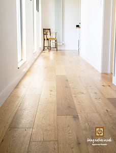 Tan coloured V4 Eiger laminate flooring in a hallway with large windows and a wooden chair at one end.