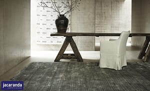 Dark grey Jacaranda Arani Iron rug in a contemporary style room beneath a wooden trestle style table.