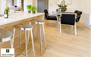 Light tan Ted Todd Fleece European Oak flooring, in a modern kitchen setting under a bar stools and dining furniture with chrome legs.