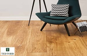 Rich tan Coloured Ted Todd Huxley European Oak flooring with wide planks, in a modern setting under a dark grey cushioned chair with wooden legs.