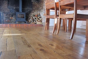 Simply Bespoke Collection flooring in a traditional style living space with a wooden dinning table and chairs in front of a wood burning stove in a large open fireplace.