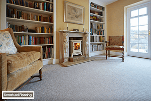Light grey coloured Unnatural Flooring Augusta New England NE6025 carpet in a traditional style living room featuring a wood burning stove in a stone fireplace.