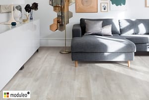 Moduleo Santa Cruz Oak 59143 flooring in a contemporary style living space with white a low backed grey corner sofa unit.