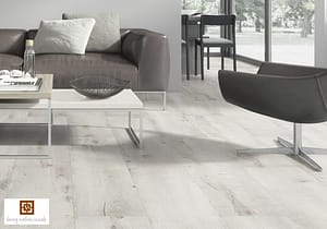 Light coloured V4 Silvered Oak Laminate flooring in a modern living room with grey shaded furniture and a low level white topped coffee table.