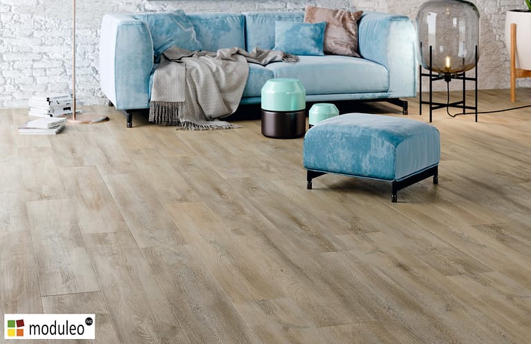 Moduleo Santa Cruz Oak 58253 flooring in a traditional style living space with a sky blue chesterfield style sofa and matching foot stool.